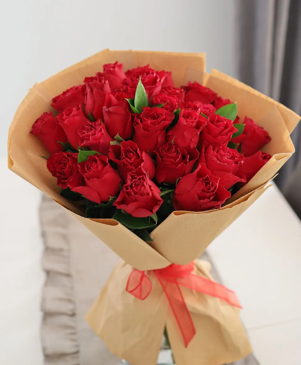 Bó hoa hồng đỏ thẫm đầy đặn với nhiều bông xếp lớp và nụ xanh, gói giấy hồng nude nhiều lớp và buộc nơ ruy băng đỏ — bó hoa 20/10 dành cho Hà Trang
